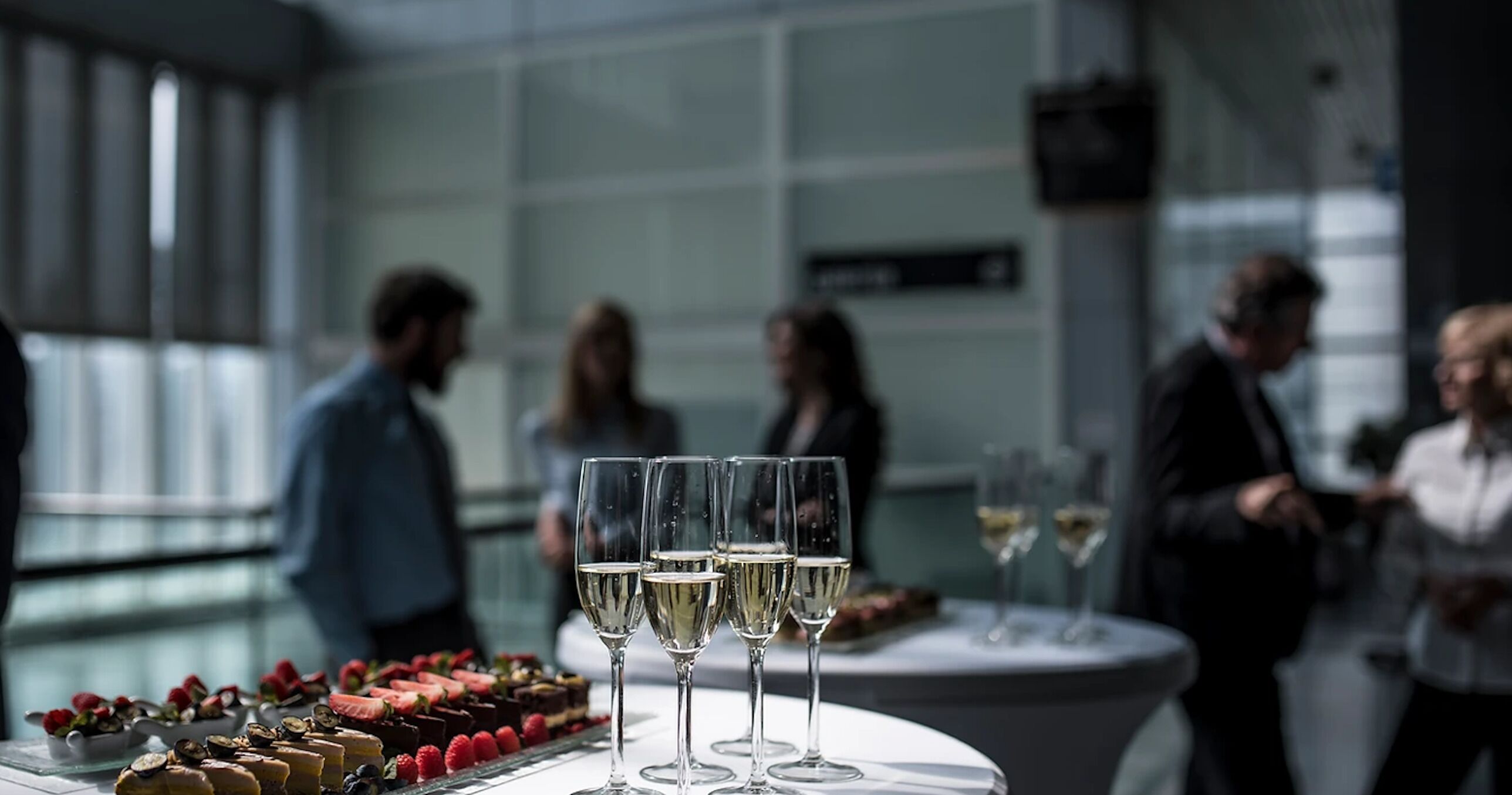 Een tafel met champagneglazen en desserts in een moderne, overdekte omgeving.