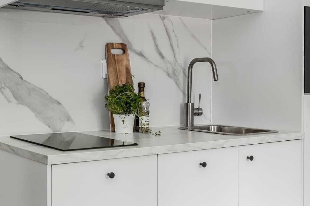 Una cocina moderna con protector contra salpicaduras de mármol, estufa empotrada, un lavabo y una tabla de cortar de madera.
