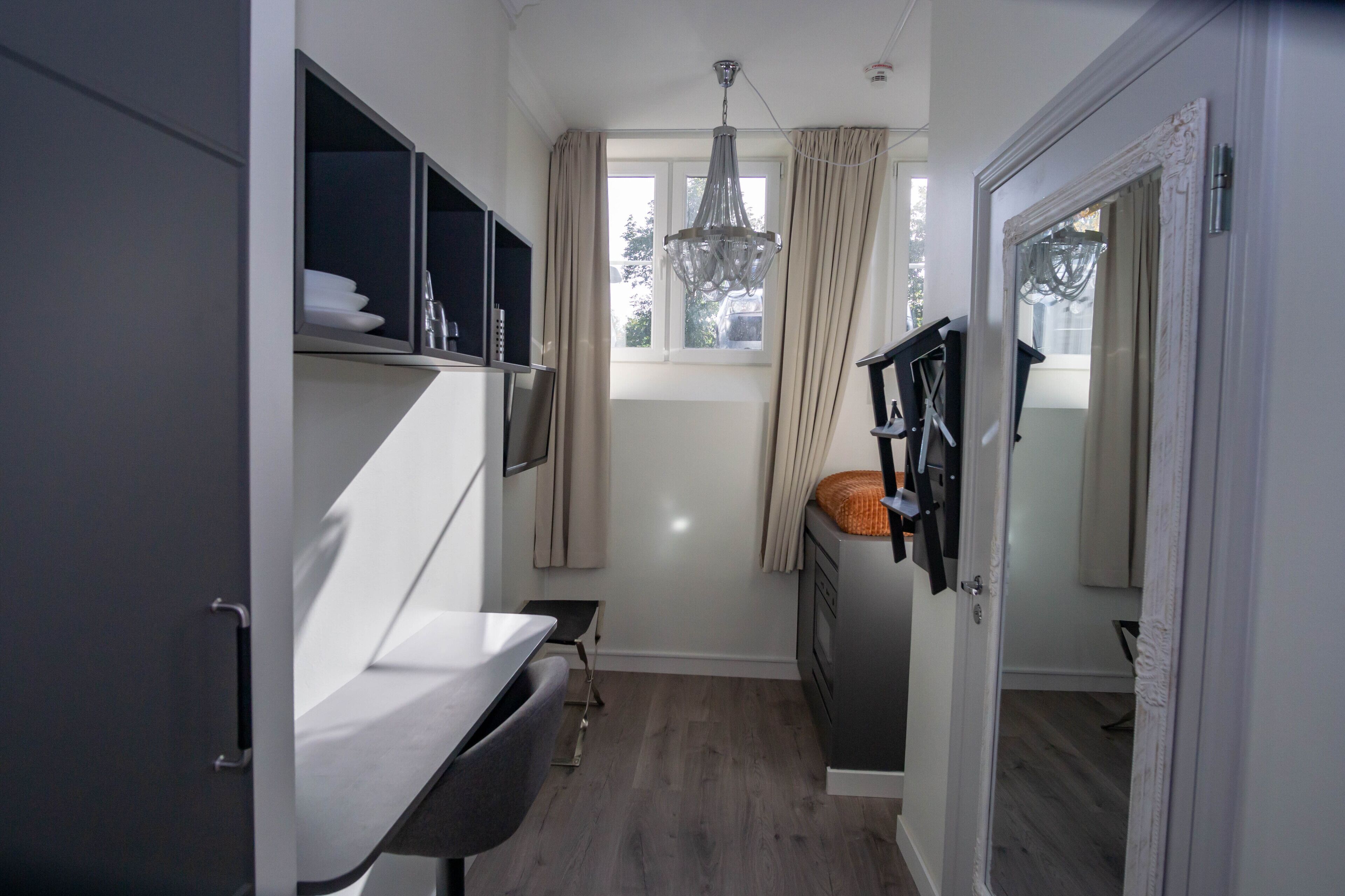 Una cocina compacta con zona de comedor, una ventana con cortinas y una puerta que da a otra habitación.