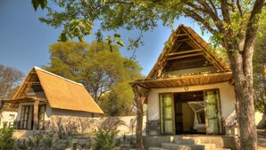 A traditional thatched-roof house with a stone foundation, a wooden porch, and a small garden with rocks and plants.