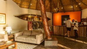 A lobby with a thatched roof, a sofa, a coffee table, and a reception desk with staff.