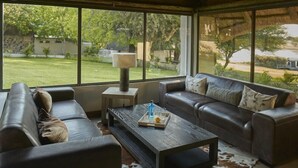 A modern living room with leather sofas, a coffee table, and a large window offering a view of a garden.