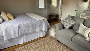 A bedroom with a bed, a grey sofa, and a woven rug.