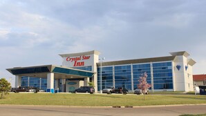 Un Crystal Star Inn con fachada de vidrio moderna, un letrero llamativo y un estacionamiento con varios vehículos.