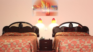 Una habitación doble con dos camas, cada una con una colcha estampada, una mesita de noche con teléfono y una obra de arte en la pared sobre las camas.