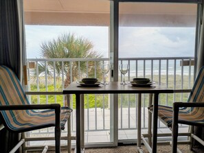 A balcony with a table set for two, chairs, and a view of the ocean.