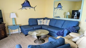 A living room with a blue sofa, a beige sofa, a glass coffee table, a small side table, and a lamp. - SUBTROPICAL PARADISE DIRECT OCEANFRONT 2/2 CONDO: STUNNING VIEWS,  HEATED POOL (Cocoa Beach)