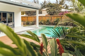 Ein modernes Haus mit Swimmingpool, einer überdachten Terrasse und einem Holzzaun.