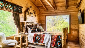 Un dormitorio rústico con cabaña de madera, una cama, una silla, una mesa y un ventanal grande.