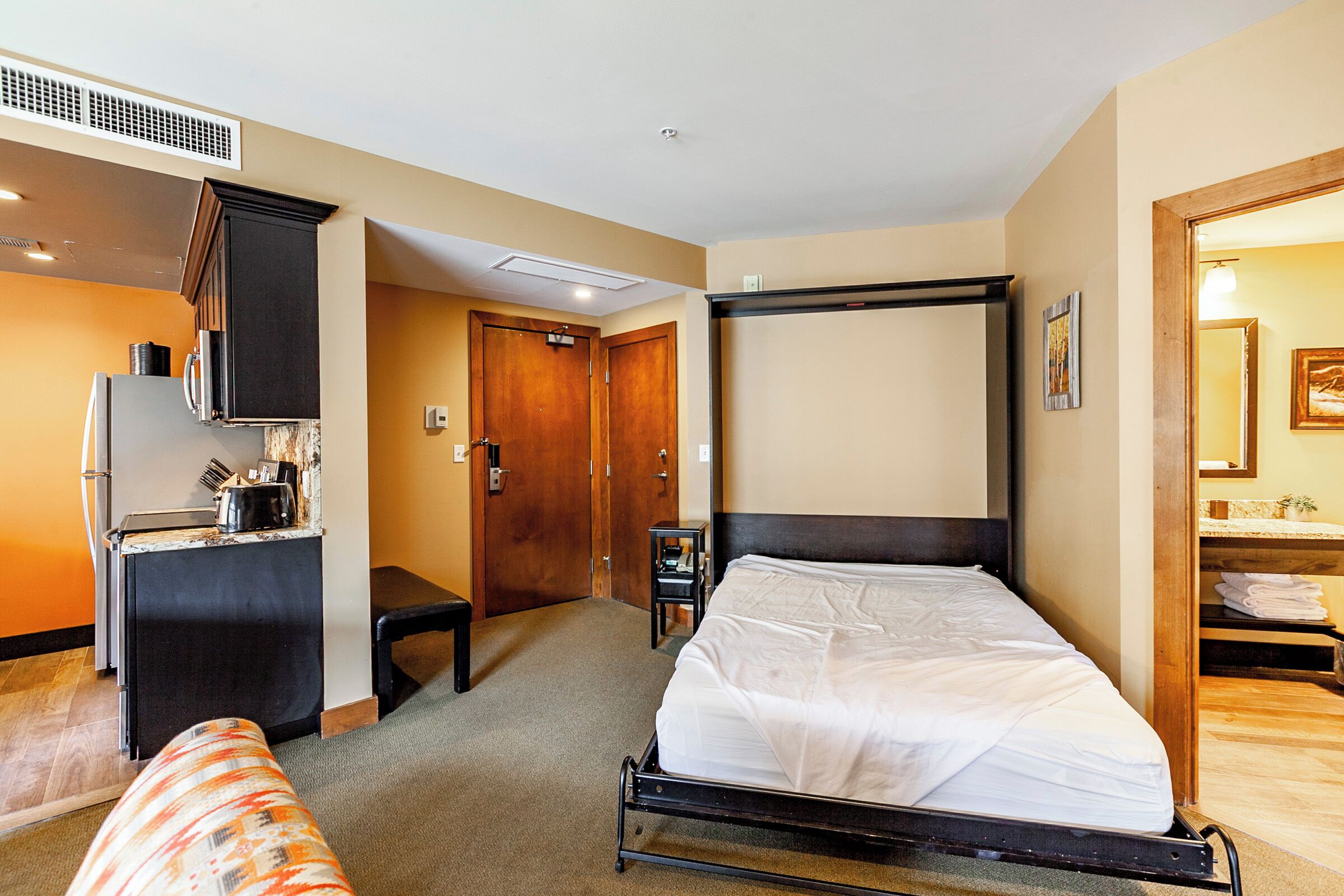 Una habitación de hotel con cama, kitchenette, baño y un pequeño rincón de descanso.