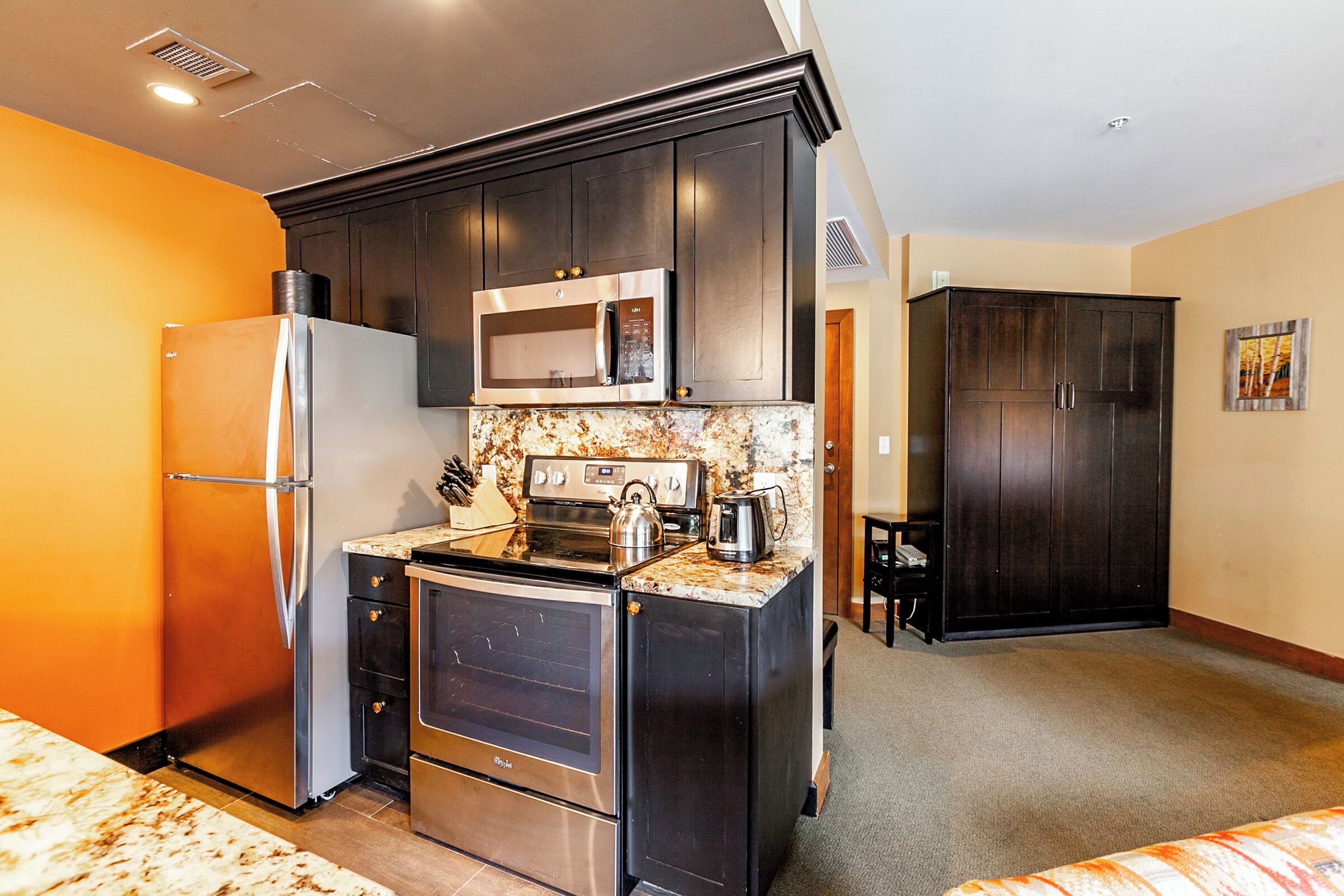 A compact kitchen with dark cabinets, a stainless steel refrigerator, a microwave, and a stove.
