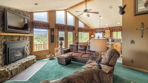 A cozy living room with a fireplace, leather sofa, and a view of the outdoors. - Amazing Views of Shadow Mnt/lake,firepit,3br/2ba Cozy Cabin in Grand Lk,sleeps6 (Grand Lake)