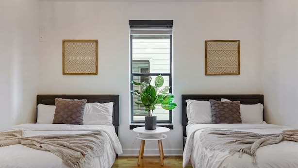 Una habitación con dos camas, una mesita redonda con una planta y decoración mural estampada.