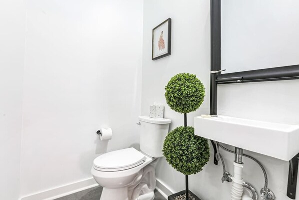 A modern bathroom with a toilet, sink, and two decorative spherical plants.