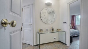 A hotel room with a glass console table, a round mirror, and a bed with a patterned bedspread.