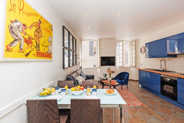 Una cocina moderna con armarios azules, un comedor con una mesa preparada para dos personas y un cartel grande en la pared.