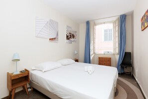 Habitación de hotel con cama, mesita de noche, lámpara, cómoda, ventana con cortinas y decoración en la pared.