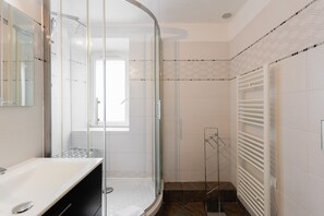 Un baño moderno con cabina de ducha de vidrio, un lavabo blanco y un perchero para toallas.