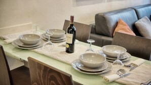 A dining table set with plates, bowls, wine glasses, and a bottle of wine, with a couch in the background.