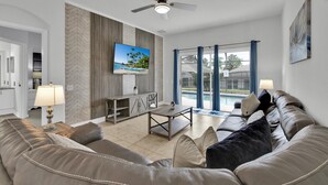 A living room with a sofa, a coffee table, a TV mounted on the wall, and a ceiling fan. - New Listing! Windsor Palms Resort, 3mi to Disney & 13mi to Universal - GRH439083 (Kissimmee)