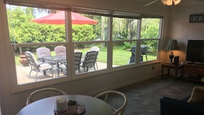 Un comedor con un gran ventanal, una mesa con sillas y un televisor sobre un mueble de madera.