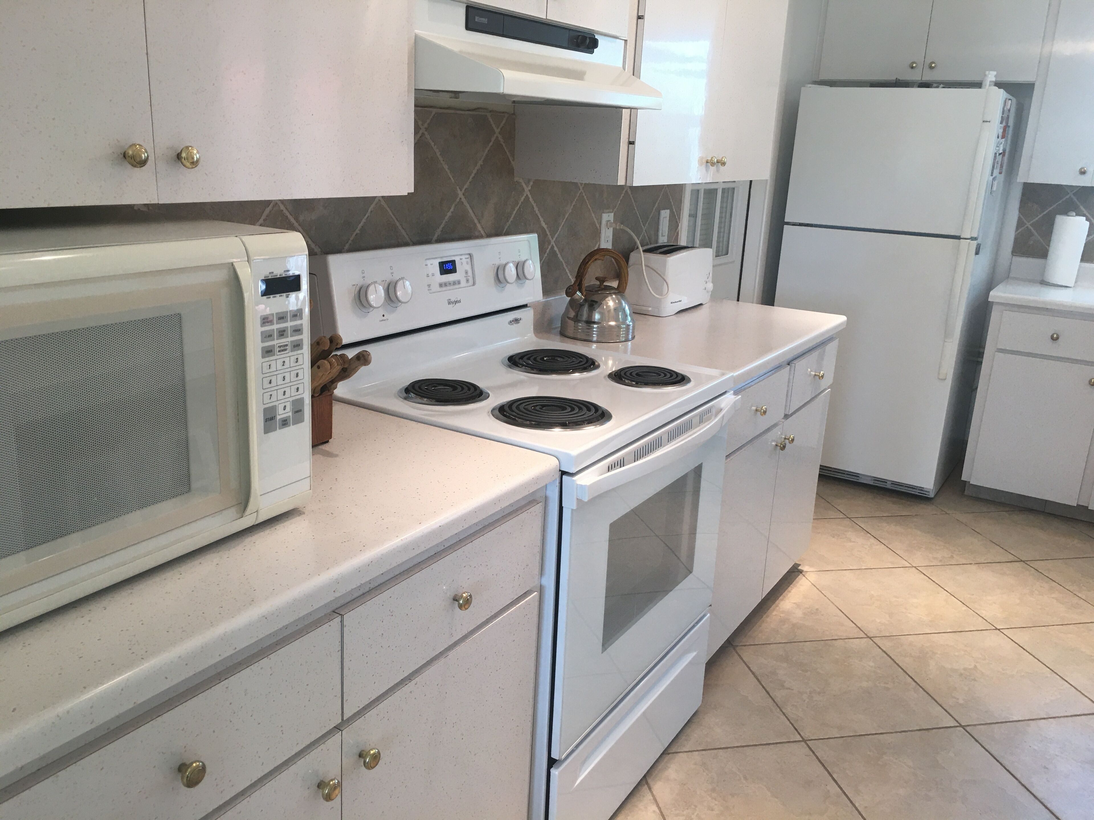 Una cucina con mobili bianchi, un forno a microonde, un fornello e un frigorifero.