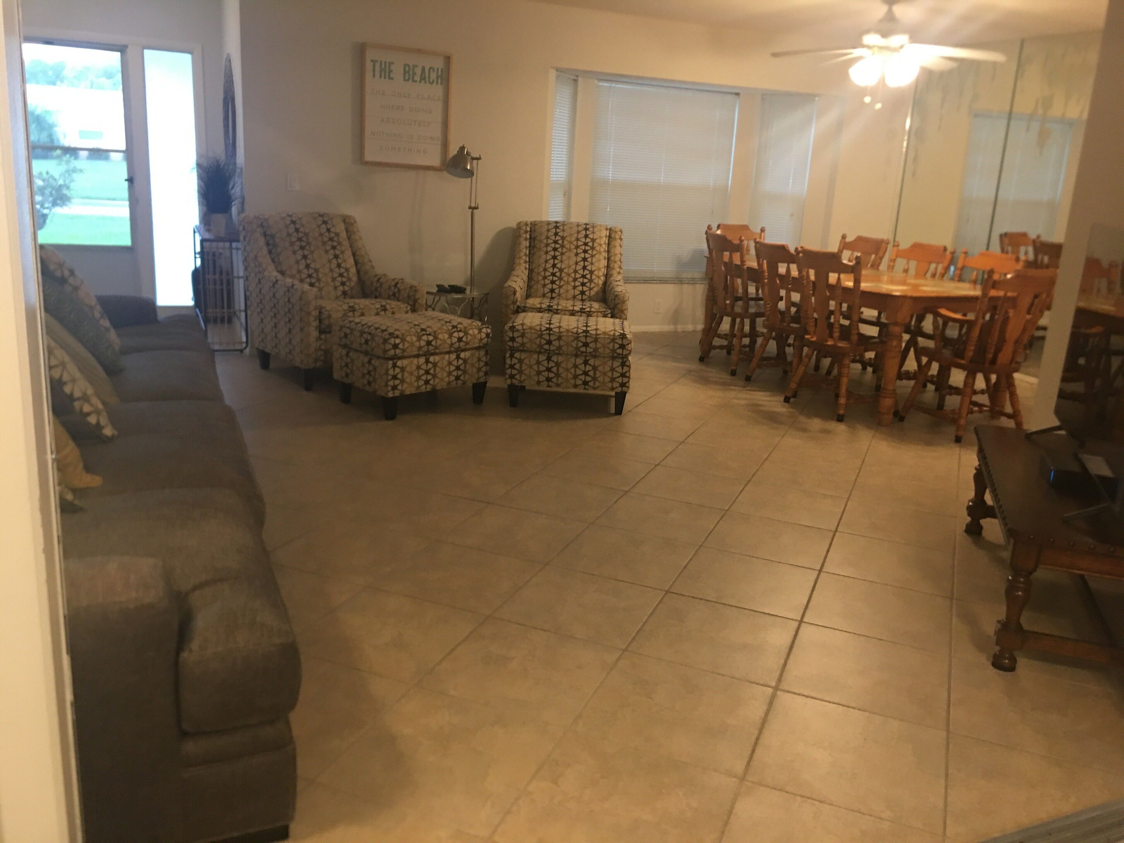 A living room with a sofa, patterned armchairs, a dining table with chairs, and a ceiling fan.