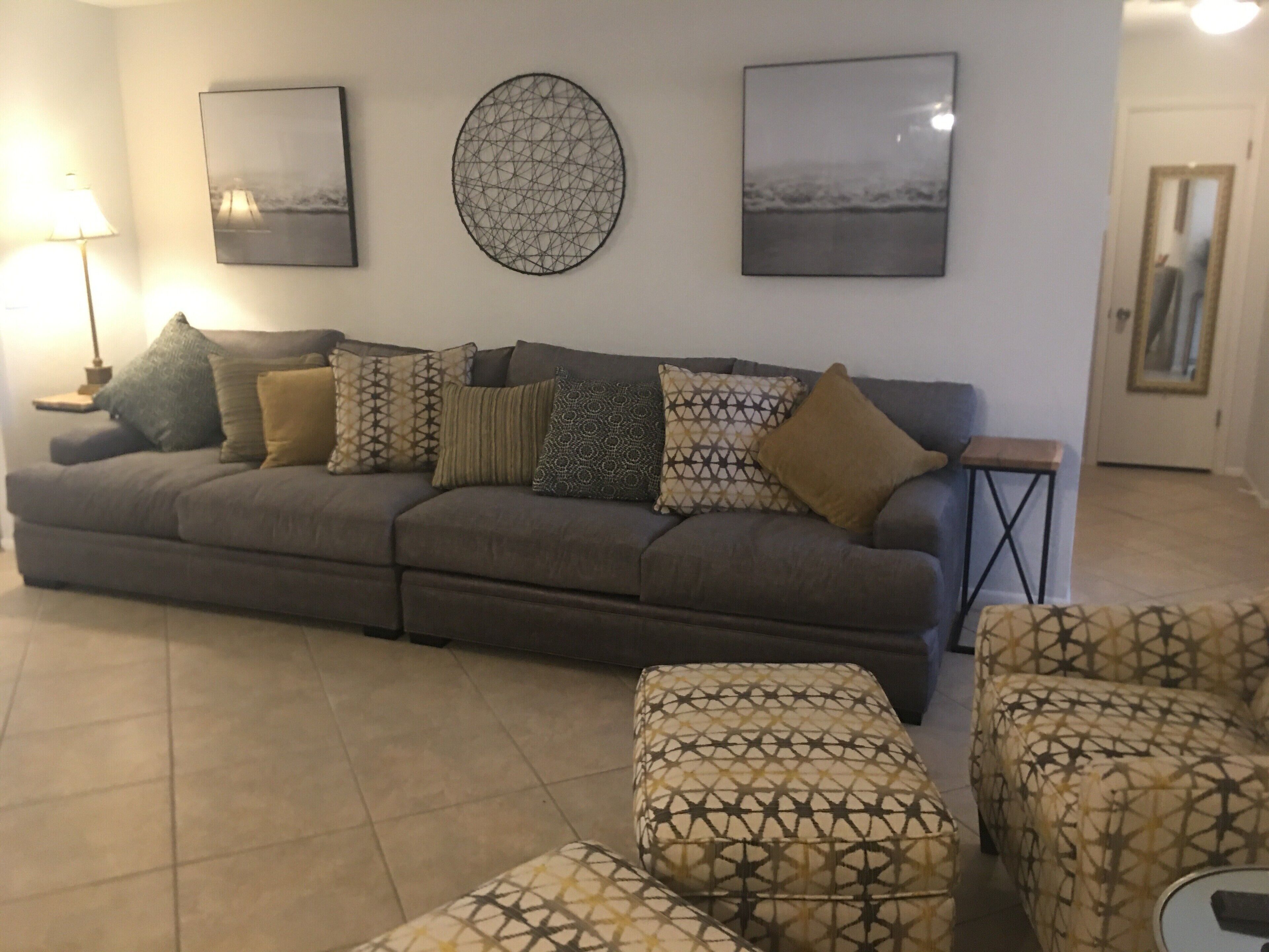Ein Wohnzimmer mit grauem Sofa, gemusterten Kissen, einer runden Wanddekoration und zwei gerahmten Bildern.