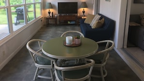 Una sala de estar con televisor, un sofá azul, una mesa de comedor con sillas y una ventana que ofrece vistas al exterior.