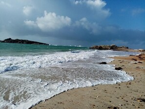 A beach with waves, pebbles, and a rocky outcrop.