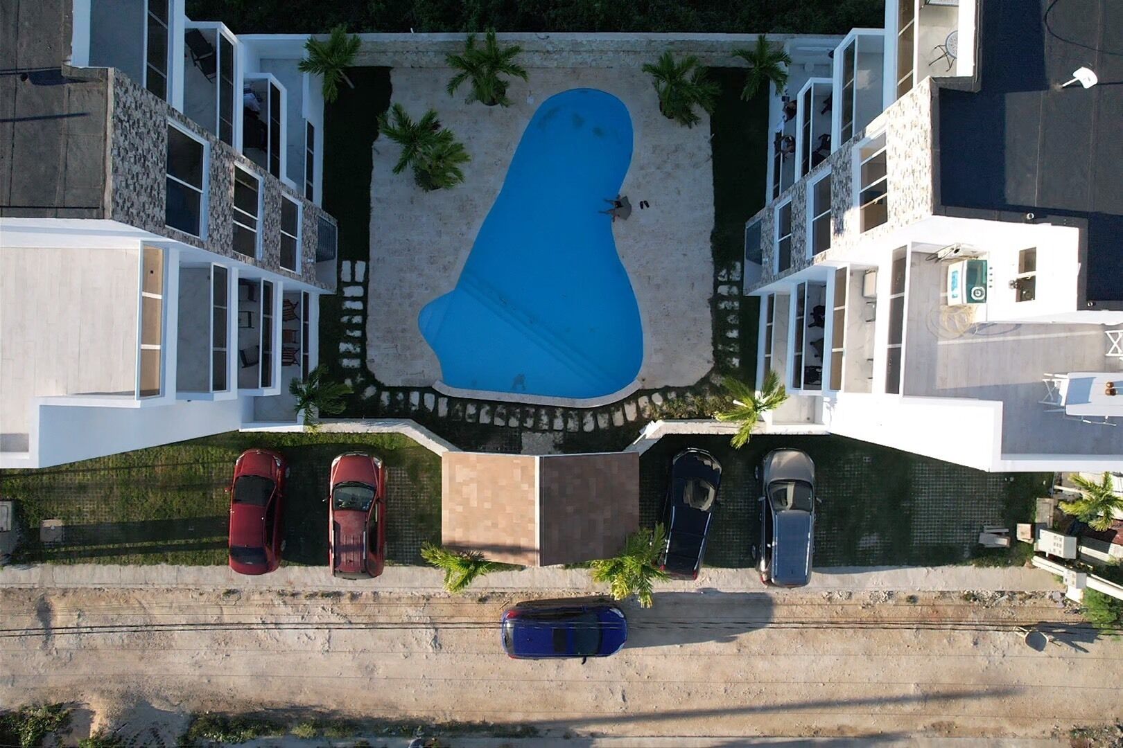 A modern building with a swimming pool, multiple cars parked in front, and a small boat docked at the pool's edge.