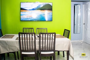 A dining area with a table set for four, chairs, a flat-screen TV on the wall, and a bright green wall.