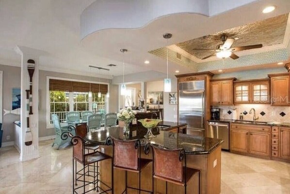 A modern kitchen with a central island, bar stools, and wooden cabinets. - Dream Home with Gulf and Intracoastal Views, Water Access (Indian Shores)