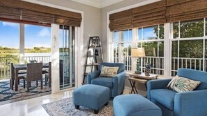 Ein geräumiges Zimmer mit großem Fenster, Deckenventilator und einer Sitzecke mit blauen Sofas und einem kleinen Tisch.