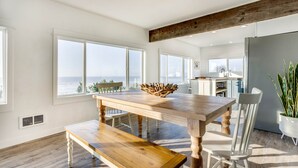 A modern kitchen with large windows, a wooden dining table, and a view of the ocean. - Ocean Front with Spectacular Views! 2 Bedroom, 2 Bath! Seal Rock! (Seal Rock)