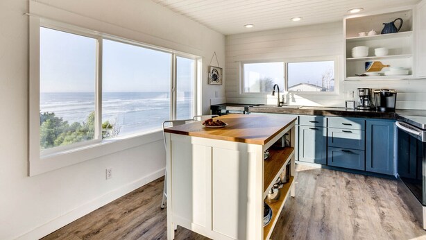 A modern kitchen with a large island, white cabinetry, and a view of the ocean. - Ocean Front with Spectacular Views! 2 Bedroom, 2 Bath! Seal Rock! (Seal Rock)