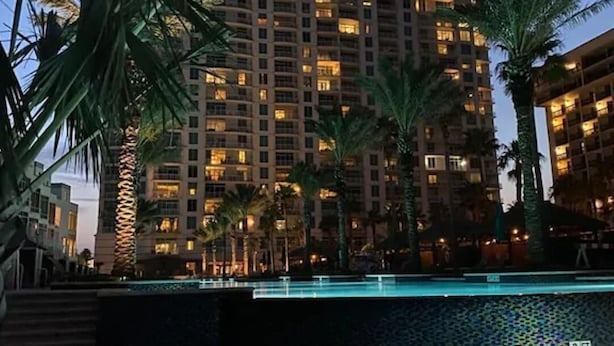 Un hotel con piscina, palmeras y edificios altos al fondo.