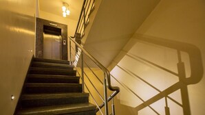 Una escalera con barandilla metálica, un letrero que indica el primer piso y una lámpara en el techo.