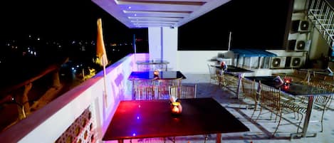 Un área de comedor al aire libre con mesas y sillas, una barandilla y vistas al cielo nocturno.
