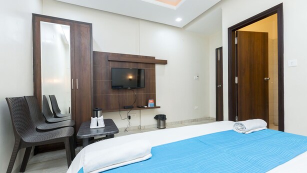 Habitación de hotel con cama, televisión montada en la pared, una silla, una mesita y una puerta.