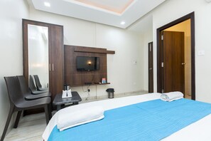 Habitación de hotel con cama, televisión montada en la pared, una silla, una mesita y una puerta.