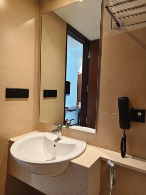 A bathroom with a white sink, a mirror, a telephone, and a shower. - OYO Premium Kakkanad Civil Station (Kanayannur)