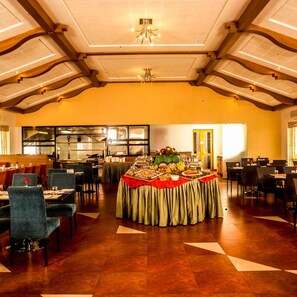 A spacious dining area with high ceilings, a central buffet table, and multiple dining tables arranged around it. - OYO Premium Kakkanad Civil Station (Kanayannur)