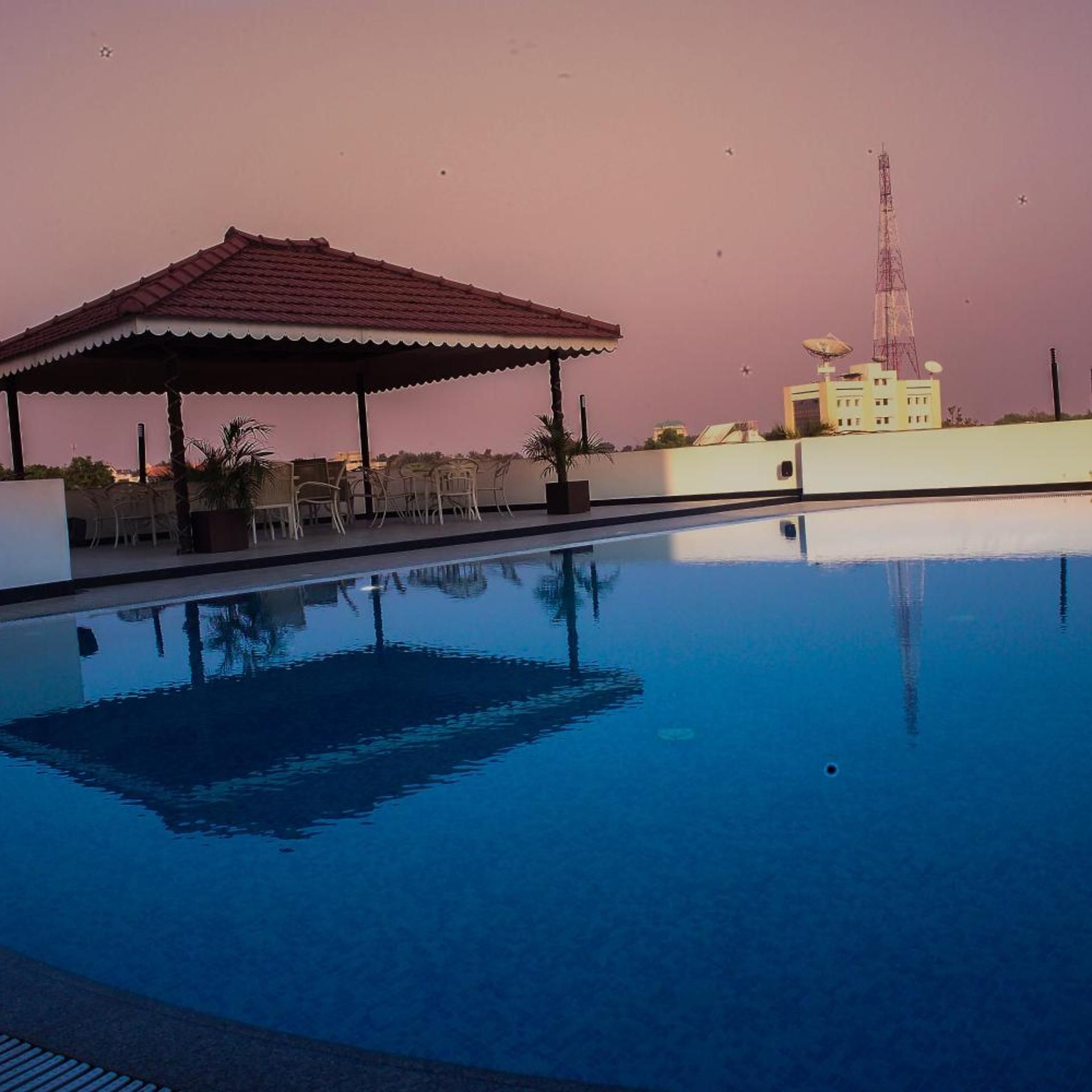 A swimming pool with a covered seating area and a building in the background.