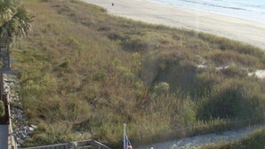 A view of a beach with a wooden walkway leading to a building with a flag. - Direct Oceanfront Corner Unit Villa, 2BR 2Bath, large pool, million dollar view! (North Myrtle Beach)
