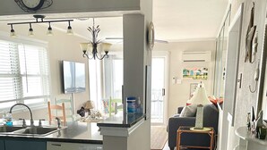 A modern kitchen with a central island, a dining area with a sofa and a coffee table, and a living room with a TV. - Direct Oceanfront Corner Unit Villa, 2BR 2Bath, large pool, million dollar view! (North Myrtle Beach)
