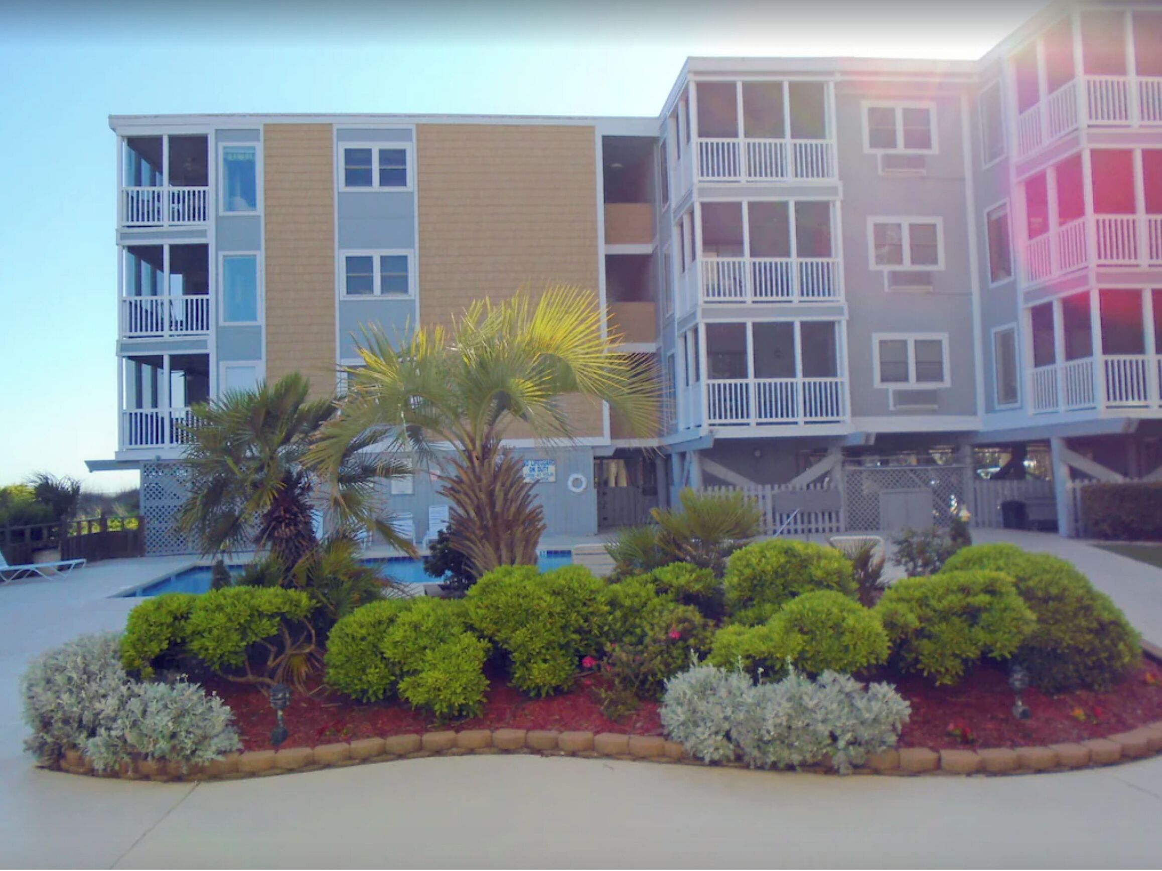 A multi-story hotel with balconies, a swimming pool, and landscaped gardens.