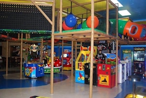 An indoor amusement area with various game machines, a climbing structure, and colorful play balls.