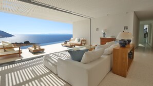 A modern living room with a large window overlooking the sea, a white sofa, a coffee table, and a wooden side table. - Luxurious Antiparos Villa with Infinity Pool and Stunning Sea and Sunset views (Antiparos)
