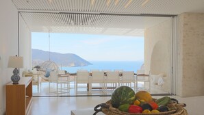 A modern interior with a view of the sea, a dining area with white furniture, and a fruit basket on a table. - Luxurious Antiparos Villa with Infinity Pool and Stunning Sea and Sunset views (Antiparos)